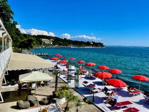 a beach with red umbrellas and chairs and the water at Hotel Riviera & Maximilian's in Trieste