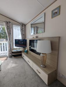a living room with a flat screen tv and a lamp at LOVELY BRIGHT AND AIRY CARAVAN ON THE 5 Star SHOREFIELD COUNTRY PARK ENTERTAINMENT PASSES INCLUDED in Milford on Sea