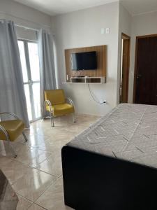 a bedroom with a bed and a tv and chairs at Residencial Nereu in Bombinhas