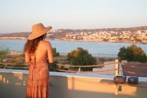 a woman in a hat standing on a balcony looking at the water at Porta Harenae Residencia in Chania