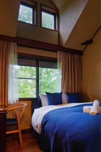 a bedroom with a bed with blue sheets and windows at Hotel Wohnen in Hakuba