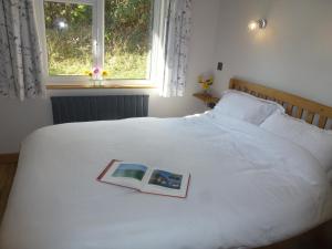 a book on a white bed with a window at Briardene Cottage - Devon countryside - sleeps 6 in Exeter