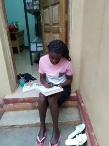 a girl sitting on the steps writing in a book at HGAD foundation in Jinja