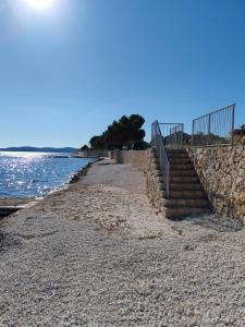 a beach with a stone wall and stairs next to the water at Seaside Serenity "Earth" with pool, 150m from sea in Sukošan