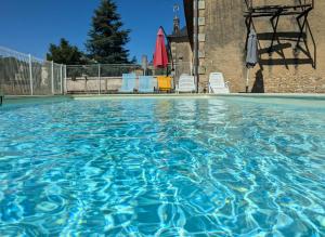 a pool of blue water with chairs and a tree at La porterie in Bignoux
