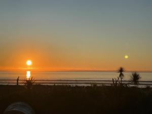 a sunset on the beach with the sun setting over the ocean at Sailor's Catch in Hokitika