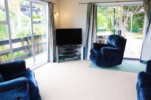 a living room with two chairs and a flat screen tv at Bobs Haven - Long Bay Coromandel in Coromandel Town
