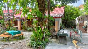 a garden with tables and benches and a tree at Khamphouy Guesthouse in Champasak
