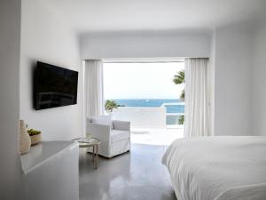 a white bedroom with a white bed and a view of the ocean at Mykonos Blu, A Grecotel Resort to Live in Psarou