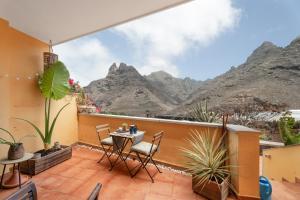 a balcony with a table and chairs and mountains at La casa de los viajeros in Punta del Hidalgo