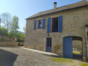 an old stone building with blue shutters and a garage at Gite de 12 personnes a molines in Saint-Étienne-du-Valdonnez