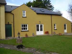 um gato preto andando em frente a uma casa amarela em The Homecoming Barn em Clogher