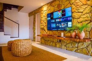 ein Wohnzimmer mit einem Fernseher an einer Steinwand in der Unterkunft Milagres Hospedagens - Casa Praia & Capela in São Miguel dos Milagres