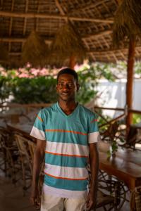 a man in a striped shirt standing next to a table at The Garden in Paje