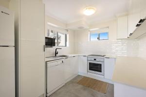 レノックス・ヘッドにあるAbsolute Beachfront Apartment 3Bのシンクと冷蔵庫を備えた白いキッチン