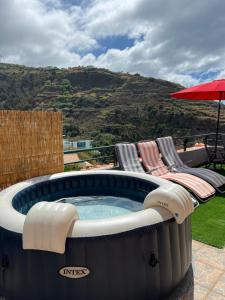 a hot tub with two chairs and an umbrella at Pana House in Calheta