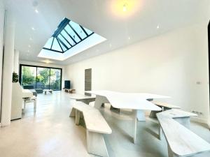 ein Raum mit weißen Tischen und Bänken und einem Oberlicht in der Unterkunft Maison de Verdure proche de Paris in Bagneux