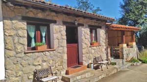 ein Steinhaus mit einer roten Tür und zwei Bänken in der Unterkunft La Casa de la Vieja in Nava