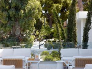 a patio with white chairs and a table and trees at The Roc Club, A Grecotel Hotel to Live in Athens