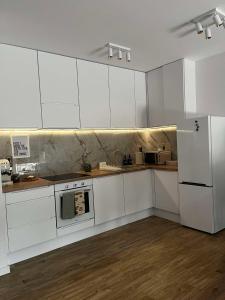 La cuisine est équipée de placards blancs, d'une cuisinière et d'un réfrigérateur. dans l'établissement Leaf Apartament Łódź prywatne miejsce parkingowe, à Łódź