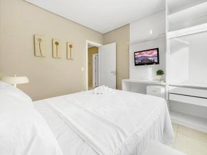 a white bedroom with a white bed and a tv at Piscina Privativa - Condominio - Churrasqueira - Espaçosa in Guarujá