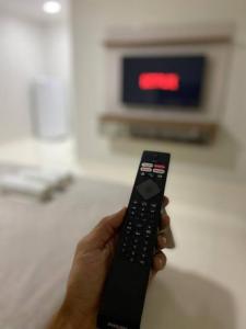 a person holding a remote control in front of a tv at Flat com 1 dormitório in Córrego da Forquiha