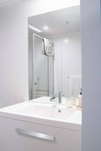 een witte badkamer met een wastafel en een spiegel bij The Downtown - A Mount Maunganui Apartment in Mount Maunganui