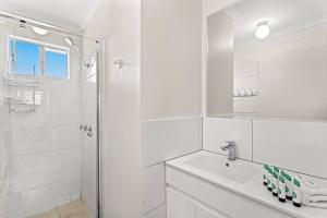 a white bathroom with a shower and a sink at Capricorn Whitsunday in Cannonvale