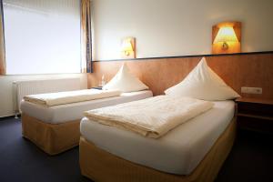 two beds in a room with two lamps on the wall at Hotel Haus Union in Oberhausen