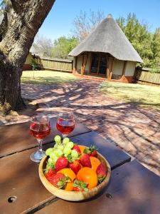 a bowl of fruit on a table with two glasses of wine at Milkwood Valley Lodge, Mabalingwe in Bela-Bela