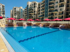 a large swimming pool with red umbrellas and buildings at ابراج الداون تاون العلمين الجديده Luxury Apartment In Downtown New Alamein in Ad Darāzīyah
