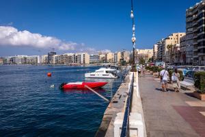 a red boat in the water next to a city at Villa on Sliema Promenade and ferries in Sliema