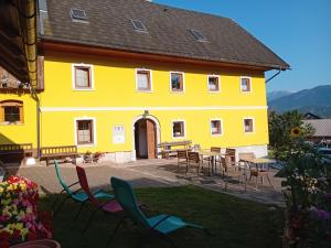 a yellow building with chairs and tables in the yard at B&B family room Tubej in Bohinj