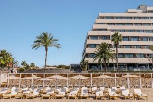 a beach with chairs and palm trees and a building at ME Sitges Terramar in Sitges