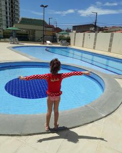 a little girl standing in front of a swimming pool at Apartamento Farolândia, Aracaju-SE in Atalaia Velha