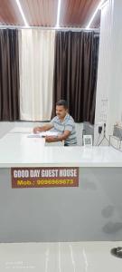 a man sitting at a desk with a sign on it at Hotel O Good Day Guest House in Alandi