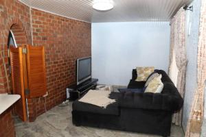 un salon avec un canapé noir et une télévision dans l'établissement Yellow Wood Cottage, à Kambanji
