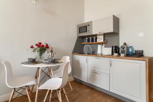 a kitchen with white cabinets and a small table with white chairs at Alpari Wawel in Kraków