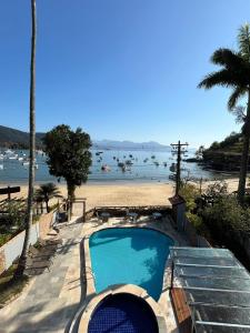 a swimming pool next to a beach with boats in the water at Pousada do Canto in Abraão