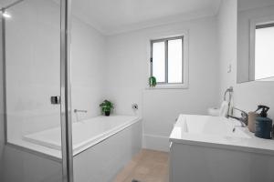 La salle de bains blanche est pourvue d'une baignoire, de 2 lavabos et d'une douche. dans l'établissement Andrica House - Your Southern Highlands Retreat!, à Mittagong
