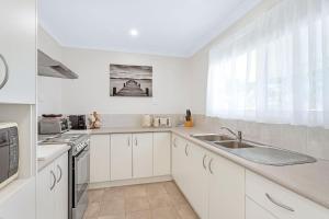 une cuisine avec des armoires blanches, un évier et une fenêtre dans l'établissement Sanctuary Cottage - Family and Pet Friendly, à Sanctuary Point 12 autres photos
