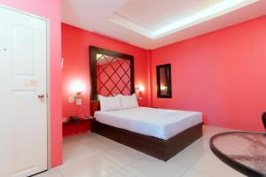a bedroom with a red wall with a bed and a table at โรงแรมนั่งเล่น in Chon Buri
