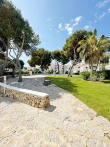 kamienna ławka w parku z drzewami i trawą w obiekcie Apartamento Lia en Port Addaia, piscina y barbacoa, perfecto para vacaciones w mieście Port d'Addaia