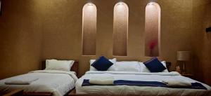 una camera con 2 letti con lenzuola bianche e cuscini blu di Omani Guest House نزل البيت العماني a Nizwa