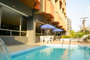 a swimming pool with tables and umbrellas next to a building at Lagoa Mar Inn - Estacionamento e duas crianças de até 10 anos Será Free in Maceió