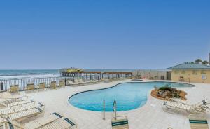a swimming pool with chairs and the ocean in the background at Ocean Views from Your Private Balcony! Sunglow Resort 907 by Brightwild in Daytona Beach Shores