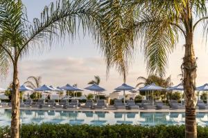 a pool with chairs and umbrellas and palm trees at Ivi Mare - Designed for Adults by Louis Hotels in Paphos