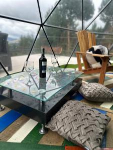 a glass table with a bottle of wine and two glasses at Glamping Terranova Guatavita Colombia in Guasca