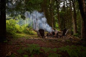 a man sitting in a hammock around a fire in the woods at Maison contemporaine Tremblant- Spa & tranquillité in Lac-Superieur