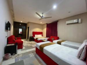 a bedroom with two beds and a red chair and couch at Hotel Tulip Inn, Gulberg in Lahore